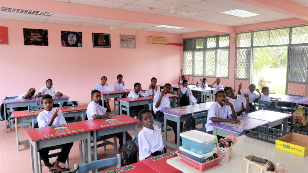 A group of Bateq tribe children sitting attentively in a brightly lit classroom.