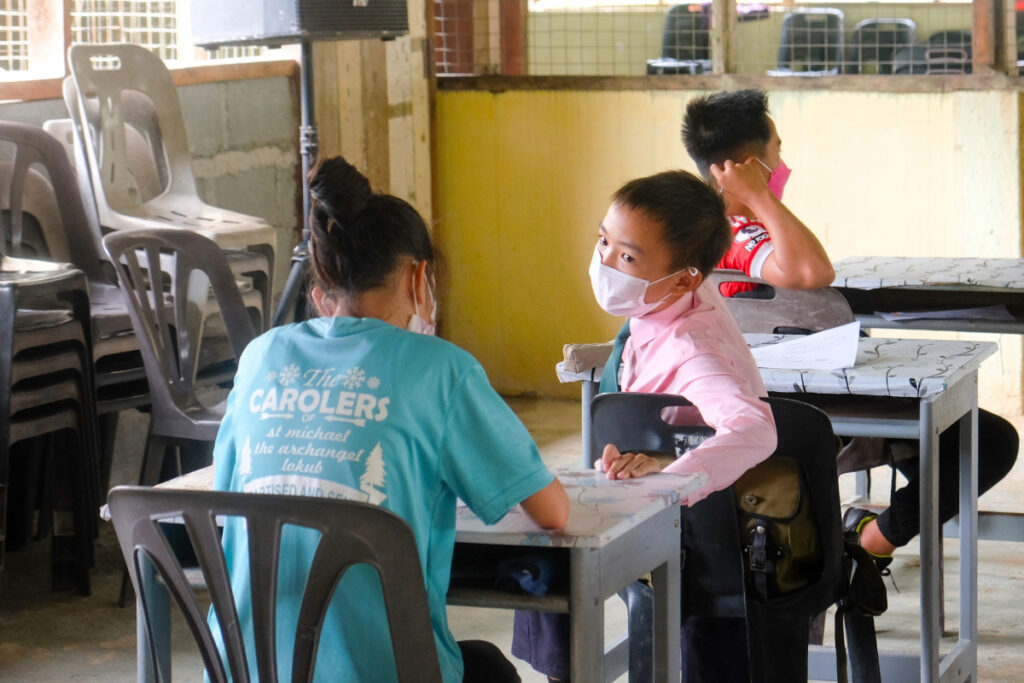 A boy turns around at his desk to talk to a girl seated behind him in a classroom during an academic support programme in Kiulu, Sabah.